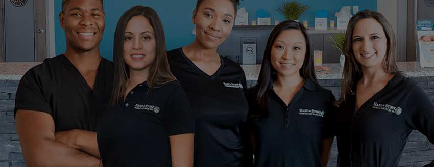 Several welcoming Hand & Stone therapists standing in front of the lobby counter in uniform.